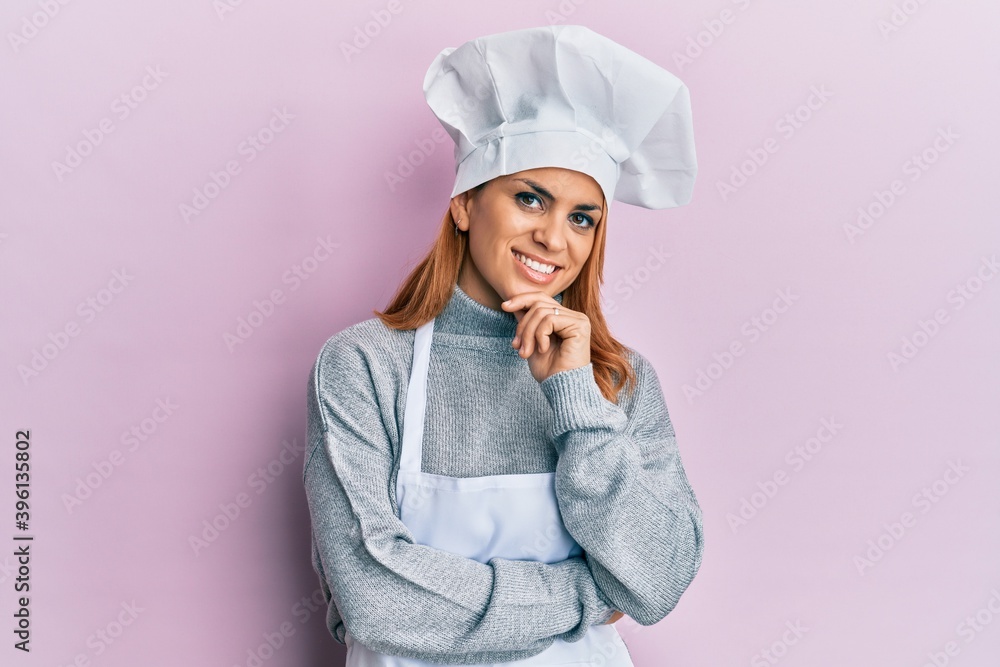 Hispanic young woman wearing professional cook uniform and hat smiling looking confident at the camera with crossed arms and hand on chin. thinking positive. Hispanic young woman wearing professional cook uniform and hat smiling looking confident at the camera with crossed arms and hand on chin. thinking positive.