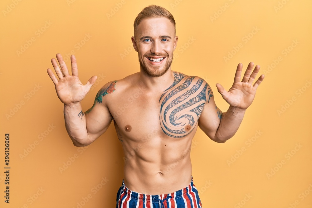 Young caucasian man wearing swimwear shirtless showing and pointing up with fingers number ten while smiling confident and happy.