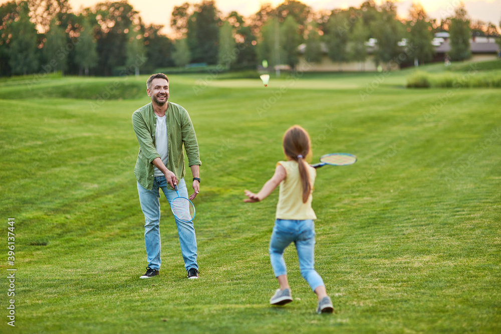 Happy father playing badminton with his joyful little daughter outdoors in the park on a summer day Happy father playing badminton with his joyful little daughter outdoors in the park on a summer day