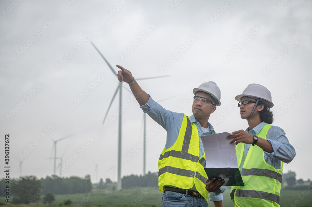 Two engineers working and holding the report at wind turbine farm Power Generator Station on mountain,Thailand people Two engineers working and holding the report at wind turbine farm Power Generator Station on mountain,Thailand people