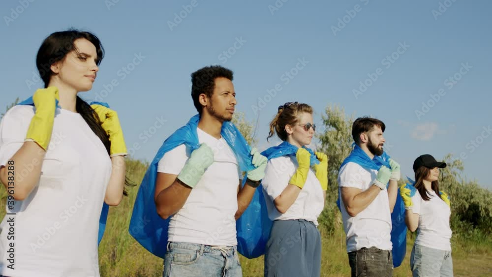 Closeup to the camera portrait of multiethnic volunteers standing on the beach side and holding blue plastic bags ready to pickup the rubbish Closeup to the camera portrait of multiethnic volunteers standing on the beach side and holding blue plastic bags ready to pickup the rubbish