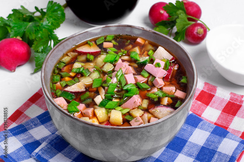 Russian cold soup Okroshka with vegetables, sausage, eggs and kvass in a bowl on the white table