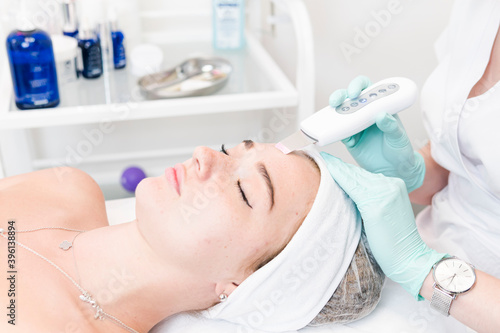 The female cosmetologist makes  a procedure of ultrasonic cleaning face, close-up. Young woman in a beauty salon.