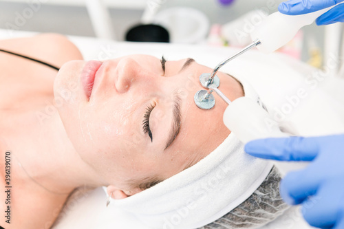 The young female client of cosmetic salon having microcurrent procedure on her face with special devices, close-up. Beautician using electrical impulses for facial procedures