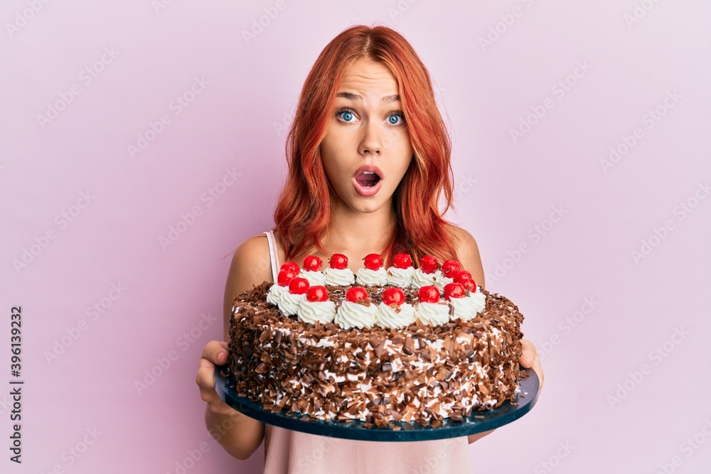 Young redhead woman celebrating birthday with cake afraid and shocked with surprise and amazed expression, fear and excited face.