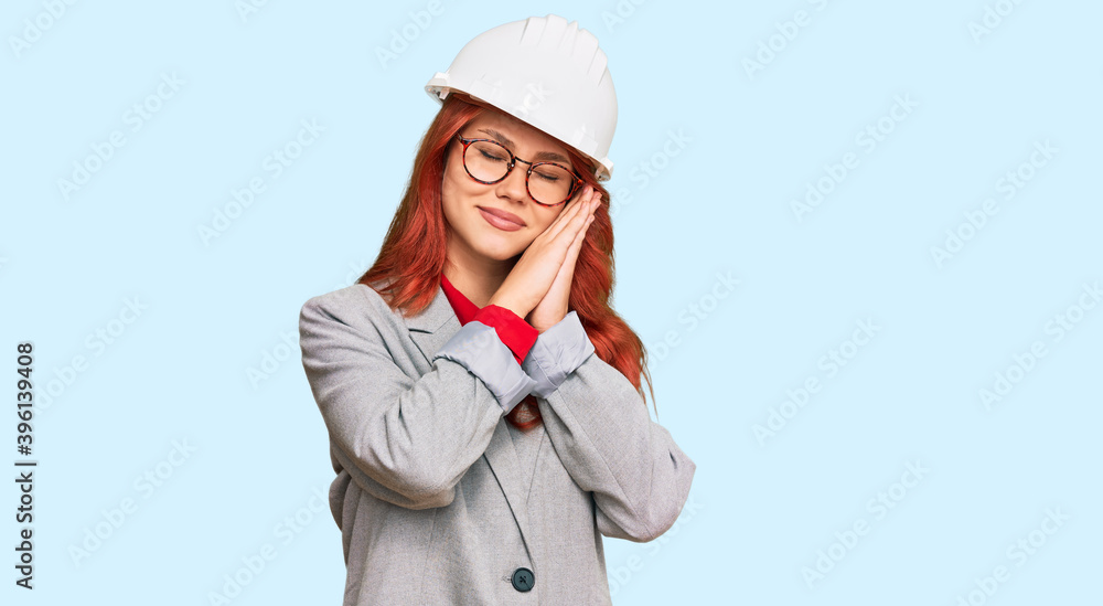 Young redhead woman wearing architect hardhat sleeping tired dreaming and posing with hands together while smiling with closed eyes. Young redhead woman wearing architect hardhat sleeping tired dreaming and posing with hands together while smiling with closed eyes.