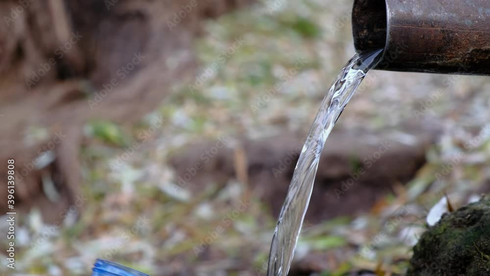 Male hiker collecting spring water from a pipe into a blue plastic