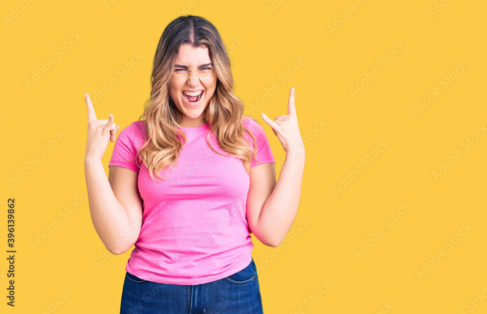 Young caucasian woman wearing sportswear shouting with crazy expression doing rock symbol with hands up. music star. heavy concept. Young caucasian woman wearing sportswear shouting with crazy expression doing rock symbol with hands up. music star. heavy concept.