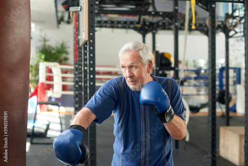 Senior man training with a punching bag. Older concentrated man boxing punching bag at gym. People, sport, active lifestyle.