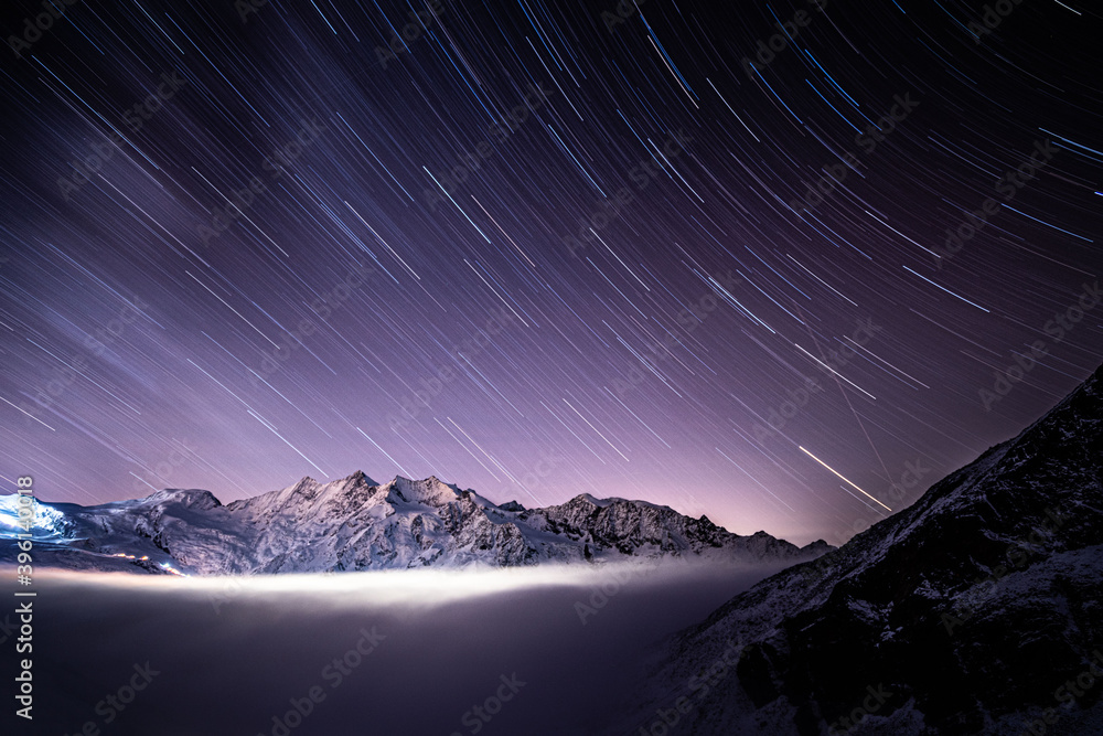 Above clouds with night sky star trails above Wallis mountains and Saas-Fee peaks, Alps, Switzerland, Europe