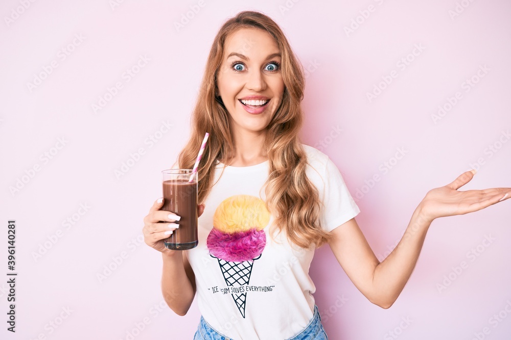 Young caucasian woman with blond hair drinking chocolate milkshake celebrating achievement with happy smile and winner expression with raised hand Young caucasian woman with blond hair drinking chocolate milkshake celebrating achievement with happy smile and winner expression with raised hand