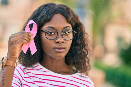 Young african american girl with serious expression holding pink breast cancer ribbon at the city.