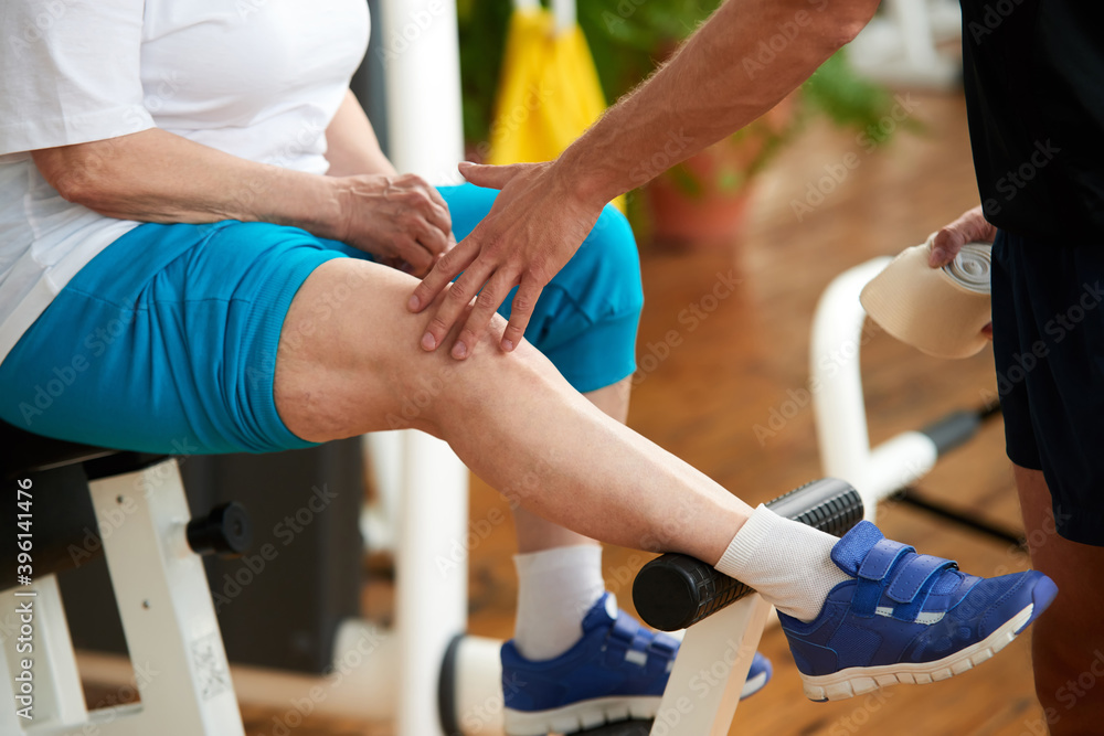 Knee pain during sport activity in gym. Trainer assisting an injured woman at gym. Injury from workout. Knee pain during sport activity in gym. Trainer assisting an injured woman at gym. Injury from workout.