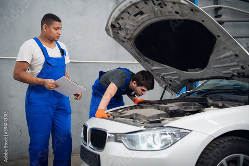 The mechanic fixing the engine of the car. His colleague writes a note