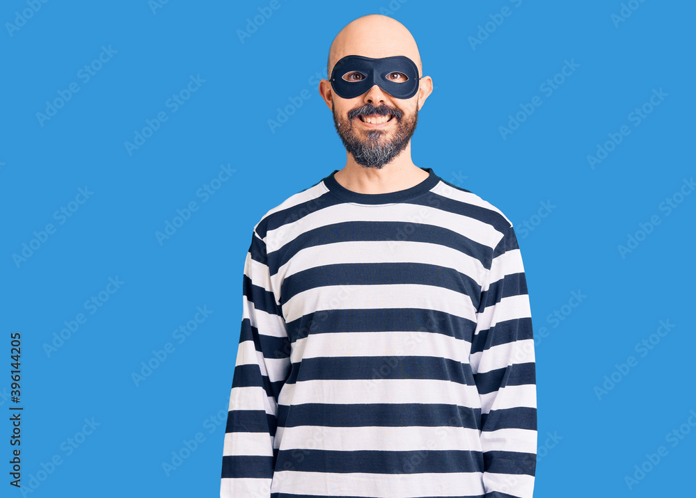 Young handsome man wearing burglar mask with a happy and cool smile on face. lucky person. Young handsome man wearing burglar mask with a happy and cool smile on face. lucky person.