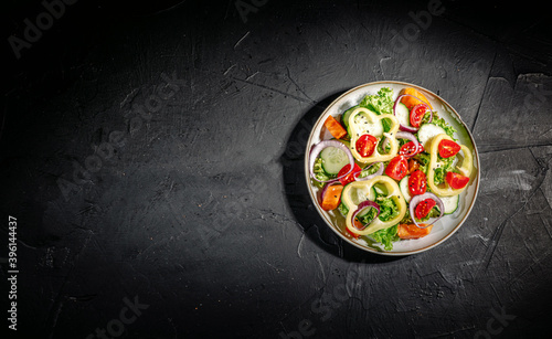 Healthy vegetable salad of fresh tomato, green leaves mix and vegetables. Top view on dark bacground. Diet menu