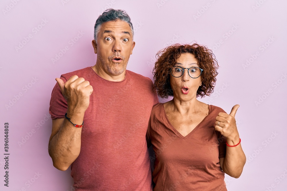Obraz premium Beautiful middle age couple together wearing casual clothes surprised pointing with hand finger to the side, open mouth amazed expression.