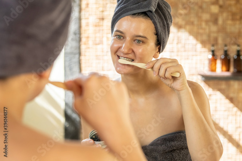Young woman with towel on head using eco-friendly oral care in bathroom- biodegradable bamboo toothbrush with charcoal solid toothpaste tablets. Zero waste and sustainable plastic free lifestyle