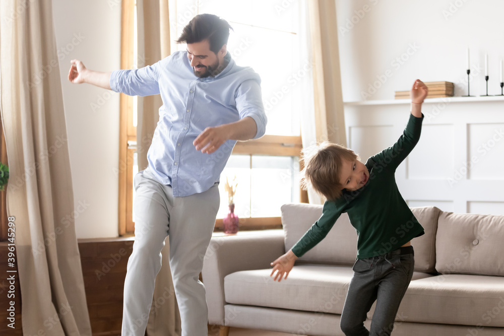Obraz premium Overjoyed young Caucasian dad have fun enjoy weekend activity with excited small preschooler son. Happy single father dance jump with little boy child, play together at home. Entertainment concept.