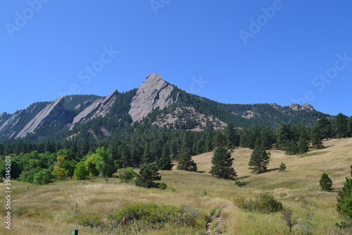 Mountain peak and ridge of the Flat Irons, with bright blue sky, pine trees and hiking trails in Boulder, Colorado.