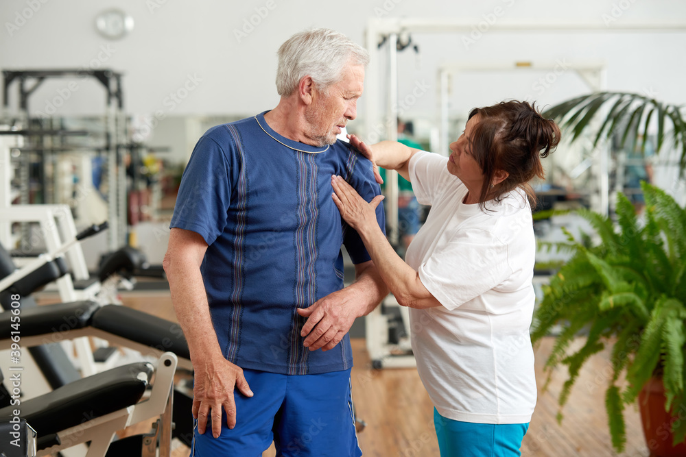 Obraz premium Senior man suffering from shoulder pain during training. Elderly people at fitness club. Old age, sport, health problem and people concept.