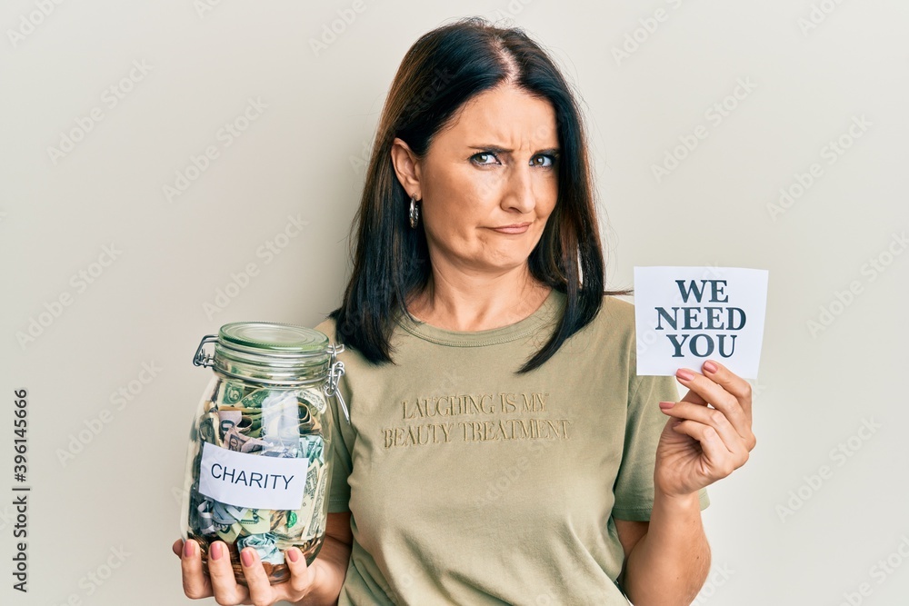 Middle age brunette woman holding charity jar with money and we need you paper skeptic and nervous, frowning upset because of problem. negative person. Middle age brunette woman holding charity jar with money and we need you paper skeptic and nervous, frowning upset because of problem. negative person.