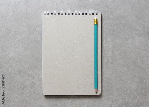 A spring notebook with a sheet of craft paper A5 with simple green graphite pencil on light grey concrete background. Concept of new idea, business plan and strategy. Empty space for text.