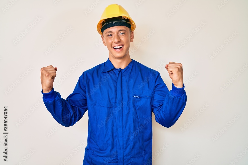 Young hispanic boy wearing worker uniform and hardhat screaming proud, celebrating victory and success very excited with raised arms