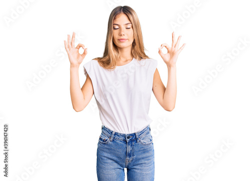 Beautiful caucasian woman with blonde hair wearing casual white tshirt relax and smiling with eyes closed doing meditation gesture with fingers. yoga concept.