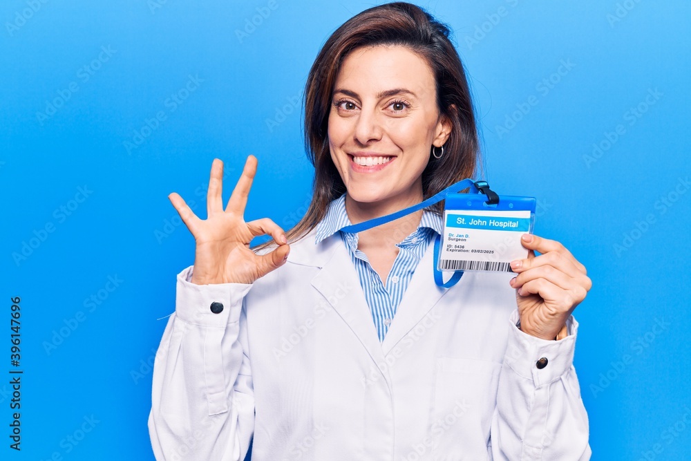 Young beautiful woman wearing doctor stethoscope holding id card doing ok sign with fingers, smiling friendly gesturing excellent symbol Young beautiful woman wearing doctor stethoscope holding id card doing ok sign with fingers, smiling friendly gesturing excellent symbol