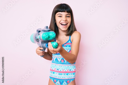 Young little girl with bang wearing swimsuit and watergun smiling and laughing hard out loud because funny crazy joke.