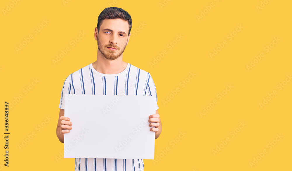 Handsome young man with bear holding blank empty banner thinking attitude and sober expression looking self confident Handsome young man with bear holding blank empty banner thinking attitude and sober expression looking self confident