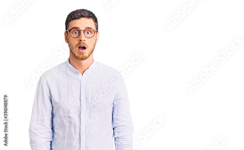 Handsome young man with bear wearing elegant business shirt and glasses afraid and shocked with surprise and amazed expression, fear and excited face.