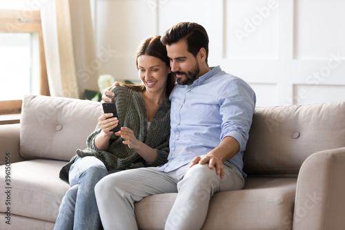 Fotografiet Smiling young man and woman sit relax on couch in living room look at cellphone screen make self-portrait picture together