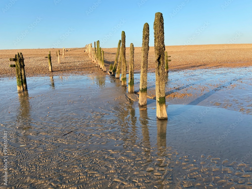 Winchelsea beach landscape view at low tide exposing flat sand with wooden sea groynes protruding from the sand close to Rye Harbour nature reserve Winchelsea beach landscape view at low tide exposing flat sand with wooden sea groynes protruding from the sand close to Rye Harbour nature reserve