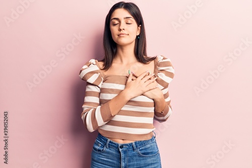 Young beautiful girl wearing casual striped t shirt smiling with hands on chest, eyes closed with grateful gesture on face. health concept.