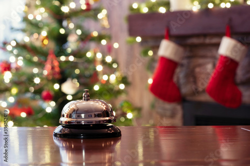 Christmas travel. Silver vintage bell on reception desk of guesthouse  and color shining garland on christmas tree on background. Hotel, restaurant.