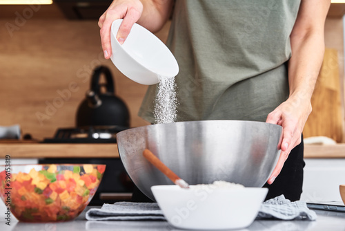 Woman in kitchen cooking a dough. Hands pour flour into a bowl