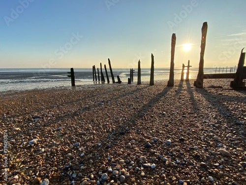 Winchelsea beach landscape view at low tide exposing flat sand with wooden sea groynes protruding from the sand close to Rye Harbour nature reserve  photo