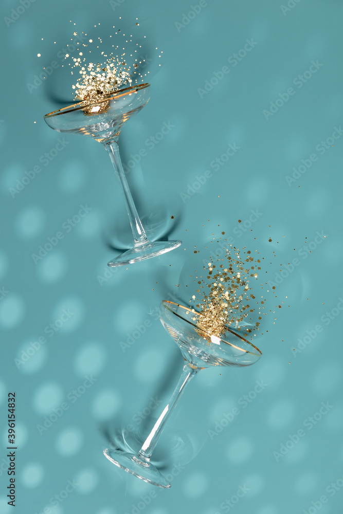 Two champagne glasses with splash of confetti over creative background