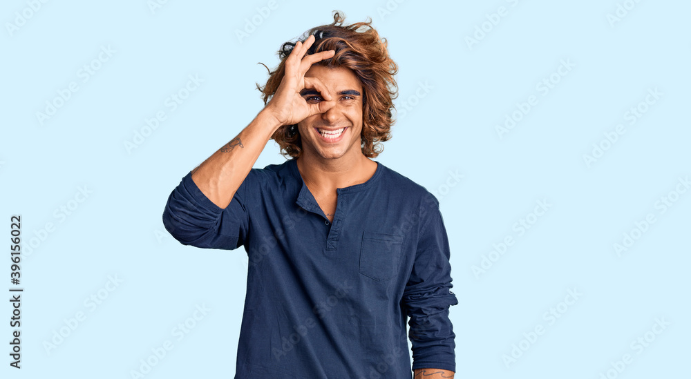 Young hispanic man wearing casual clothes doing ok gesture with hand smiling, eye looking through fingers with happy face. Young hispanic man wearing casual clothes doing ok gesture with hand smiling, eye looking through fingers with happy face.