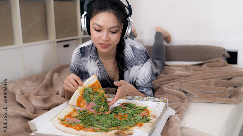 Young woman lying on the bed eats pizza - home shooting