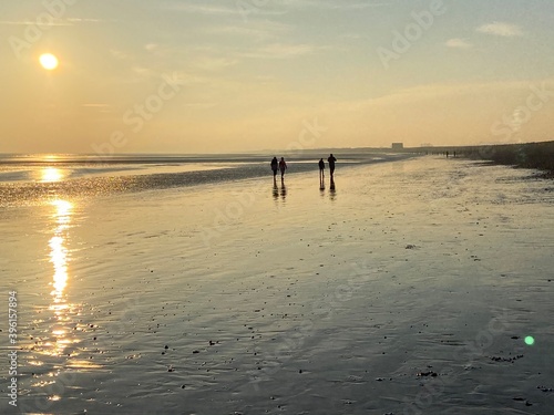 beach walk at sunset people walking reflected on wet sand beach at Wichelsea beach East Sussex UK