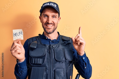 Handsome policeman wearing uniform and bulletprof holding reminder with help message smiling happy pointing with hand and finger to the side photo