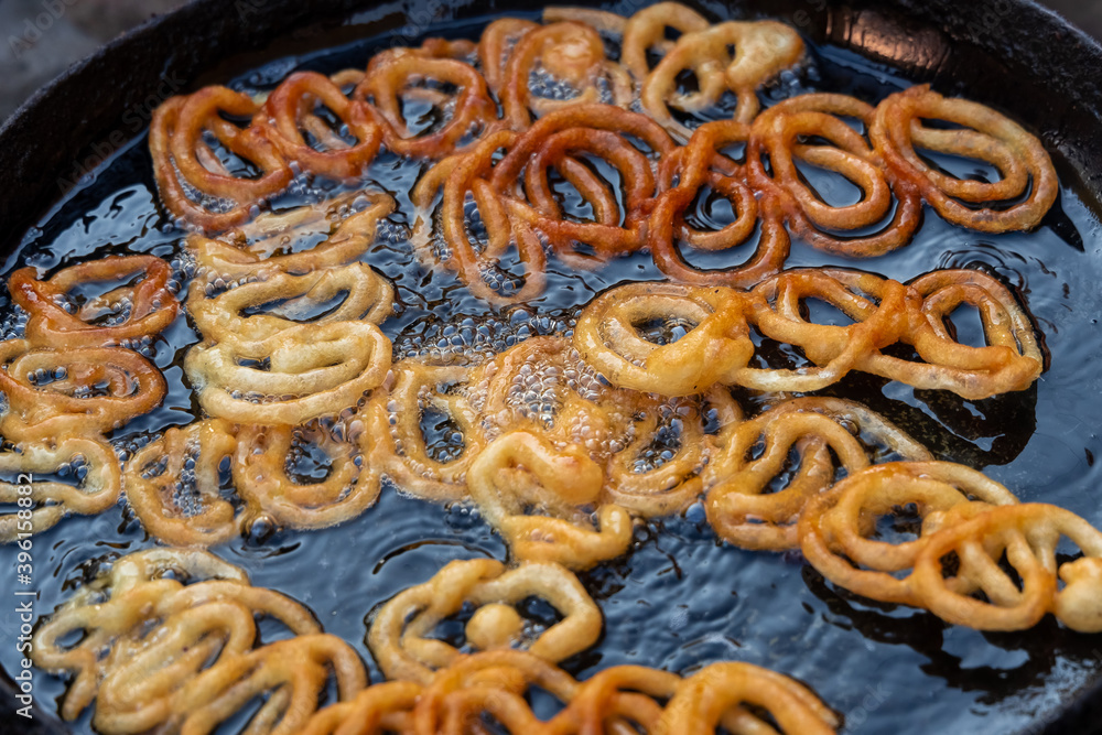 Frying Jalebi batter in oil. Red and orangecolored batter will be