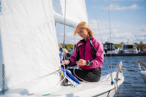 Women's river regatta on a sunny day. A young blonde sets up the rigging and secures the genaker sail before the start of the competition