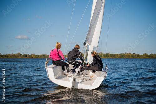 A beautiful white yacht is sailing in the wind on the river against the background of a beautiful autumn forest. A guy on board with two girls