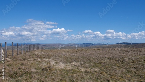 Wind farm and peat land on top of Scottish hills under blue sky with little fluffy clouds