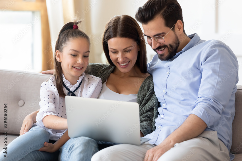 Happy young parents with little daughter rest on couch in living room browse wireless internet on laptop together. Smiling Caucasian family renters use modern computer at home. Technology concept. Happy young parents with little daughter rest on couch in living room browse wireless internet on laptop together. Smiling Caucasian family renters use modern computer at home. Technology concept.