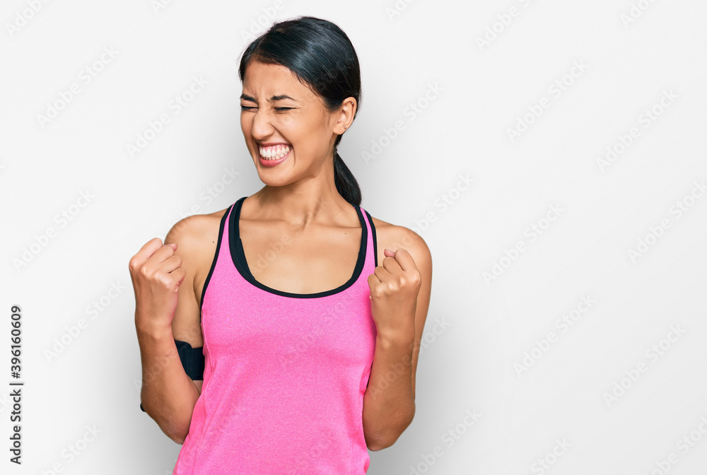 Beautiful asian young sport woman wearing sportswear and arm band excited for success with arms raised and eyes closed celebrating victory smiling. winner concept. Beautiful asian young sport woman wearing sportswear and arm band excited for success with arms raised and eyes closed celebrating victory smiling. winner concept.